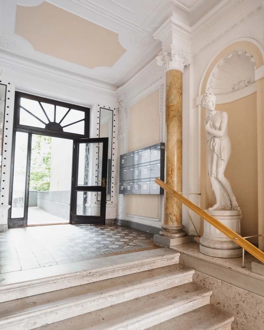 Historisches Treppenhaus mit klassischer Statue, Marmorsäule, Briefkästen und Eingangstür.